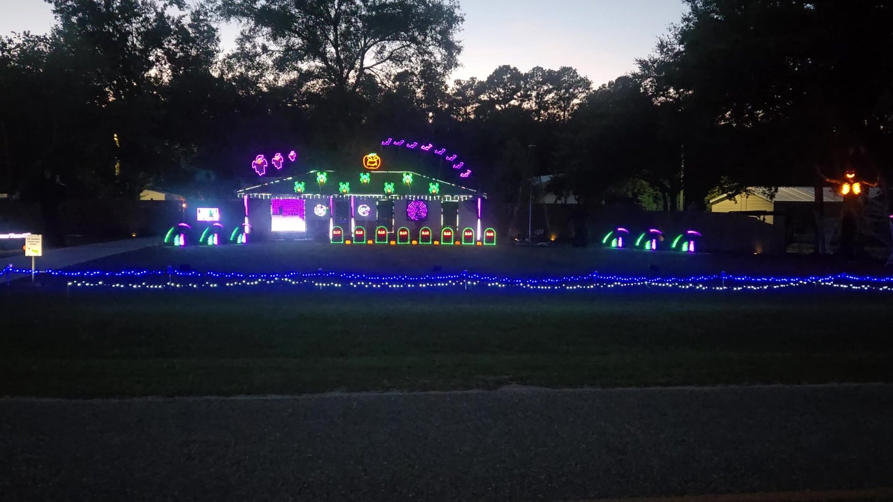 GreenWood Lights Halloween show at dusk — pixel house, pumpkin, and tombstones on County Road 24.